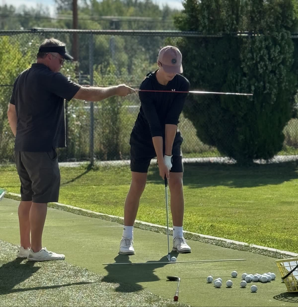 In-person golf lesson in Kelowna — Steve Lawrence coaching a student one-on-one at Kelowna Driving Range, setting his shoulder line with an alignment stick